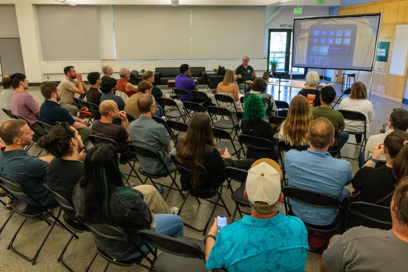 A full room on folding chairs, watching a builder talk through a programmable keypad shown on the projector screen.